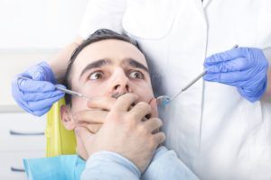man with dental anxiety covering his mouth in the dentist chair